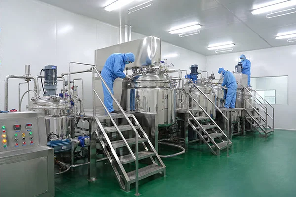 Workers in blue protective suits operating large stainless steel equipment in a cleanroom pharmaceutical production facility.